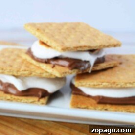 Three smores, perfectly roasted in the oven, with chocolate and marshmallow nestled between graham crackers on a white plate.