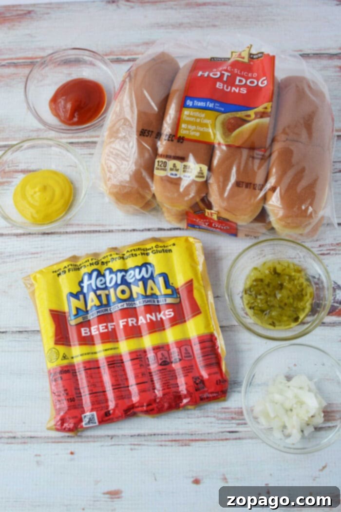 Perfect Oven Baked Hot Dogs 3 Baked Hot dog ingredients including buns, beef franks, ketchup, mustard, relish, and chopped onions on a wooden surface, ready for assembly