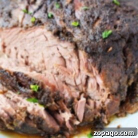 Close-up of a seasoned, sliced roast beef on a white plate, reminiscent of how to make fall-apart brisket in the oven, garnished with chopped herbs.