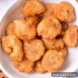 A bowl of golden-brown beer batter shrimp fritters sits enticingly on a white plate.