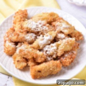 A plate of crispy banana tempura dusted with powdered sugar sits elegantly on a white plate atop a yellow cloth, ready to be served as a delightful Asian dessert.