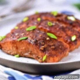 Close-up of Hot Honey Salmon grilled to perfection, garnished with green onions on a white plate.