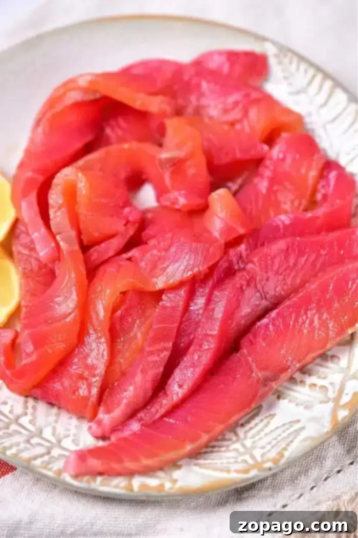Mastering Salmon Curing 2 Slices of smoked salmon are artfully arranged on a white plate with lemon wedges on the side, offering a perfect presentation to showcase your skills in mastering how to cure salmon.