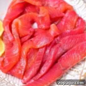Slices of raw salmon rest elegantly on a patterned plate, accompanied by lemon wedges. Discover how to cure salmon for an enhanced flavor experience.