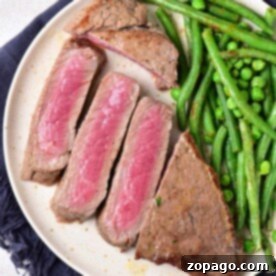 Sliced medium-rare chuck steak with green beans and peas on a white plate, resting on a dark napkin.