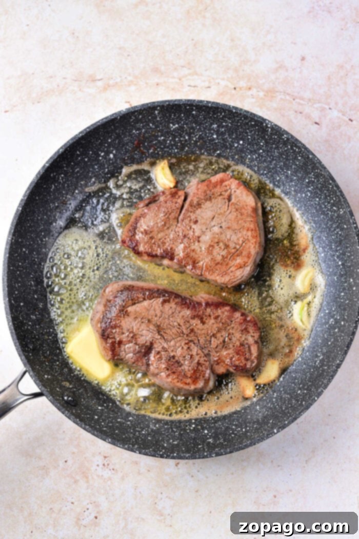 Perfectly Seared Beef Tenderloin Medallions 3 Steak medallions sizzling in a hot cast iron pan, showing a beautiful golden-brown sear and developing crust.