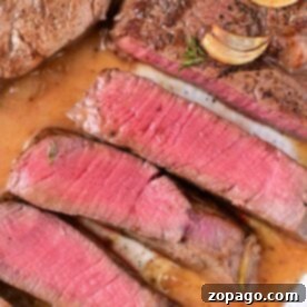 Sliced medium-rare steak with garlic and seasoning on a plate, showcasing perfectly cooked beef tenderloin medallions.