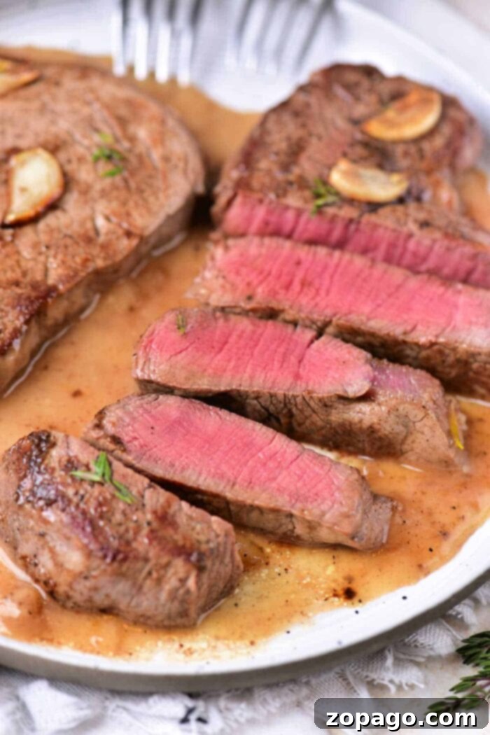 Perfectly Seared Beef Tenderloin Medallions 7 A beautifully garnished plate of sliced medium-rare beef tenderloin medallions with fresh garlic, rosemary, and thyme, ready for serving.