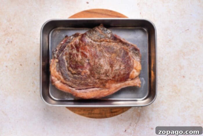 New York Strip Steak 4 Perfectly cooked medium-rare strip steak, resting in a metal roasting pan on a rustic wooden board, ready to be sliced and served.
