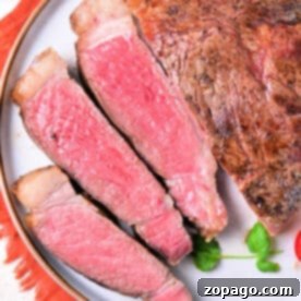 Sliced medium-rare New York strip steak on a white plate, ready to serve, representing the culmination of the oven cooking method.