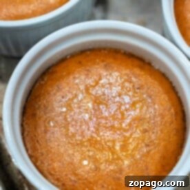 A close-up of a crustless pumpkin pie in a white ramekin, featuring a perfectly golden-brown top.
