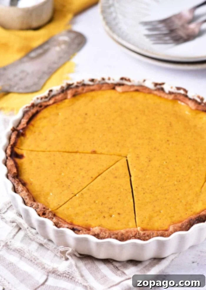 Classic Southern Sweet Potato Pie 2 A golden-brown sweet potato pie in a white fluted pie dish, with a slice removed, resting on a soft cloth napkin. A silver pie server and plates with forks are visible in the tastefully blurred background, inviting guests to enjoy this delicious Southern classic.