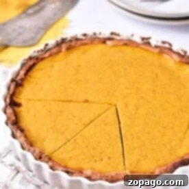Classic Southern Sweet Potato Pie 8 A sweet potato pie with a golden-brown crust and a smooth, vibrant filling sits in a classic white fluted pie dish. A single slice has been expertly cut and slightly separated, revealing the pie's tempting interior. In the soft background, additional plates, forks, and a pie server are visible, arranged on a beige cloth, hinting at a shared, delightful meal.