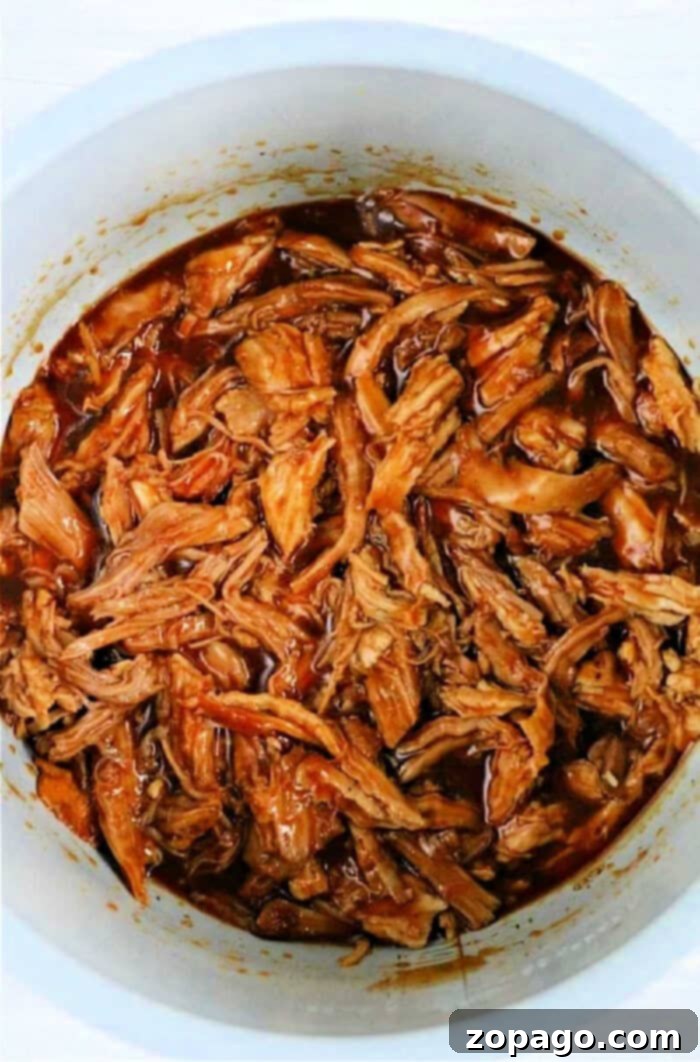 Pork Loin Leftover Creations 4 Shredded barbecue pork in a white pot, covered in rich, dark sauce, reminiscent of those delicious leftover pork loin recipes.