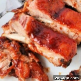 Close-up of glazed, barbecued ribs on a white plate with a fork, showcasing the perfect leftover ribs recipe.