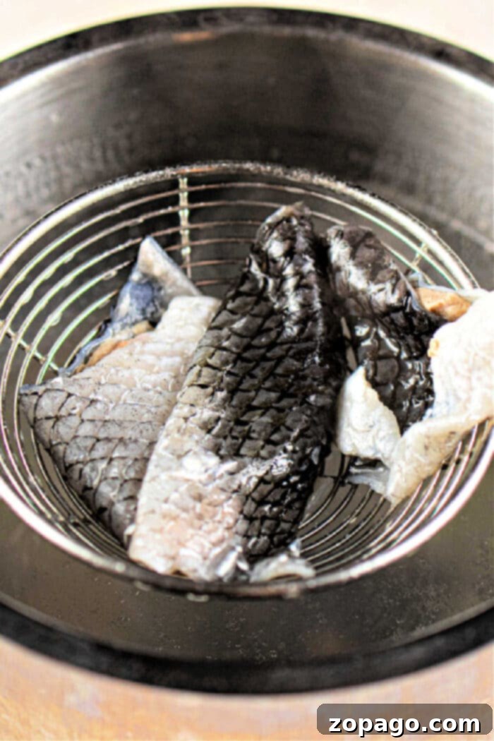 Crispy Fish Skin Delights 6 Carefully placing freshly fried crispy fish skins into a wire strainer to drain excess oil over a metal pot.