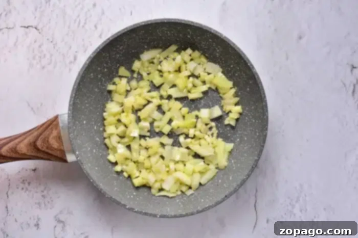 Crispy Stuffing, Baked Separately 4 Chopped onions are being sautéed in a non-stick frying pan with a wooden handle on a light textured surface, perfect for adding that savory touch to your oven-baked stuffing.