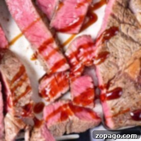Melt-in-your-mouth, sliced medium-rare steak with sauce drizzled on top, served on a white plate with a black fork.