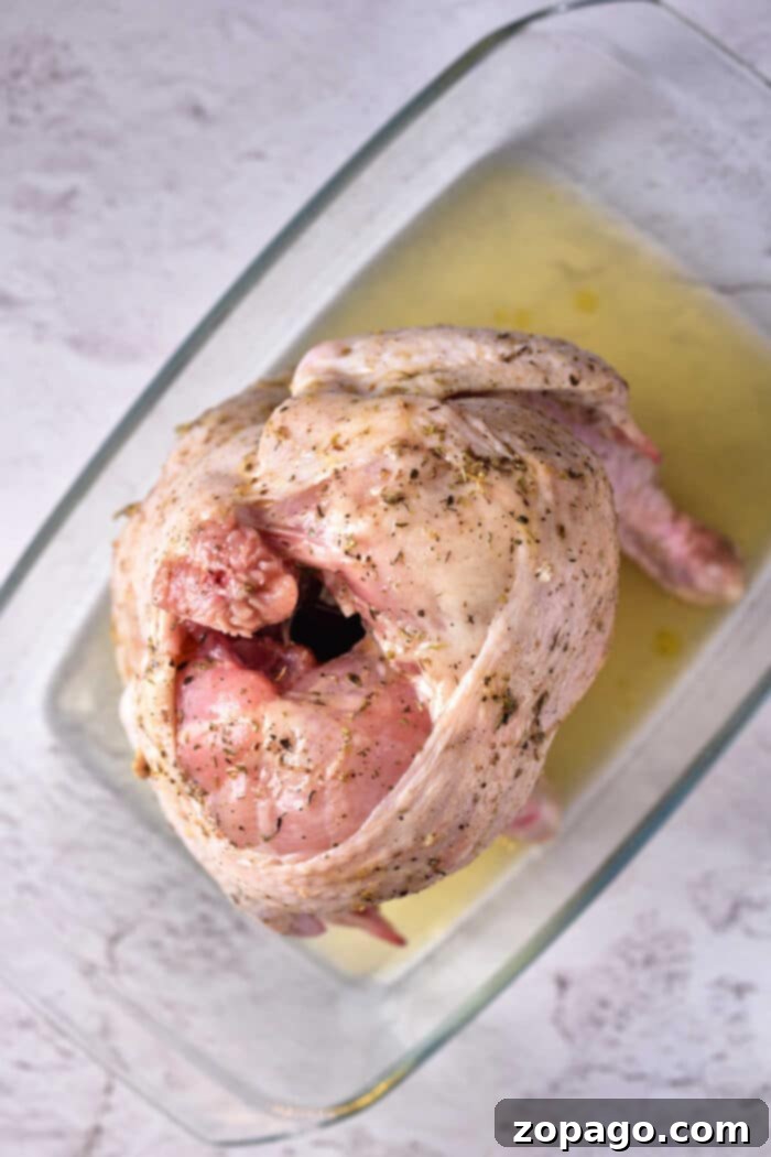 Raw seasoned Beer Can Chicken in the Oven, sits ready in a glass baking dish on a light surface.