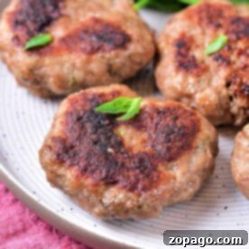 Easy Oven-Baked Sausage Patties 7 Sausage patties cooked to perfection, resting on a white plate with fresh greens in the background, bring an inviting aroma from the oven.