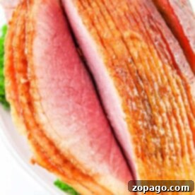 Close-up of a sliced, glazed ham served on a platter with parsley garnish, showcasing the delightful results of how to cook a spiral ham in the oven.