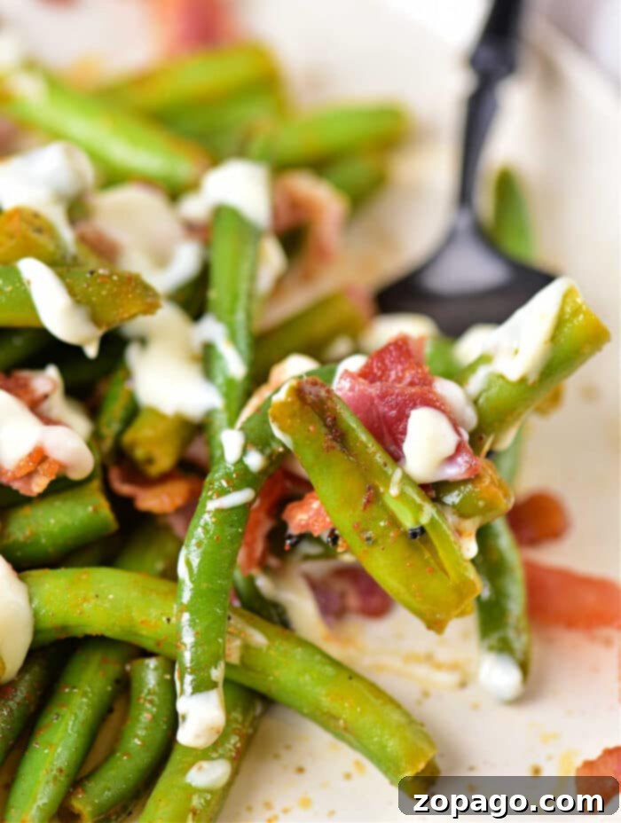 Irresistible Green Beans 8 Overhead shot of a serving of Crack Green Beans with bacon on a white plate, highlighting the rich sauce.