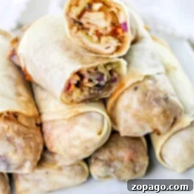 A stack of air fryer spring rolls filled with vegetables sits enticingly on a white plate, showcasing a perfect blend of crispiness and flavor.