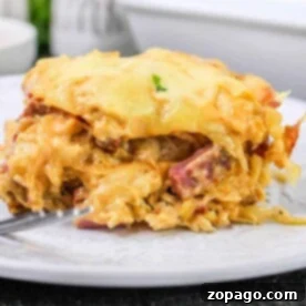 A cheesy layered Corned Beef Casserole with tender meat and colorful vegetables, elegantly presented on a pristine white plate.