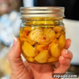 A hand holds a glass jar filled with fragrant garlic cloves immersed in rich garlic oil.