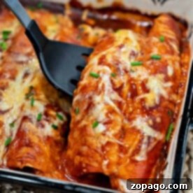 Close-up of cheesy rotisserie chicken enchiladas in a baking dish, topped with melted cheese and chives, with a spatula serving them.