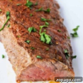 Perfect Oven Roasted Tri Tip 7 Grilled steak, reminiscent of how to cook tri-tip in the oven, is seasoned with herbs and spices, garnished with parsley, on a white plate.