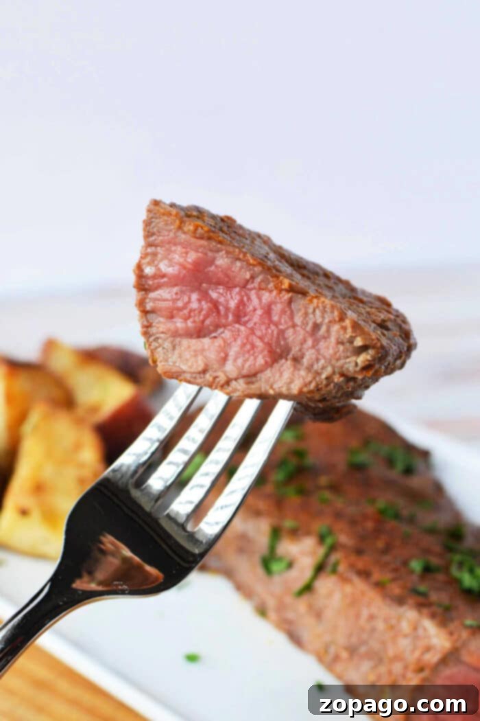 Perfectly Tender Oven Tri Tip 4 A fork holds a piece of juicy, medium-rare tri tip steak above a plate featuring steak and roasted potatoes. Learn how to cook tri-tip in the oven for this succulent result.