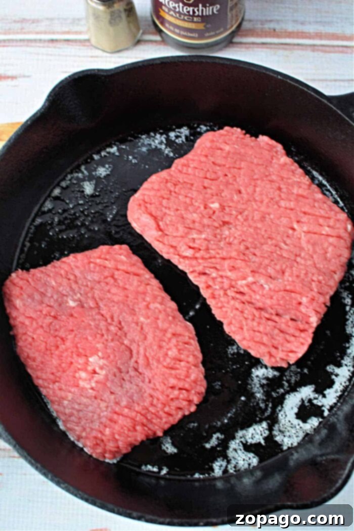 Frying Pan Cube Steak: Master the Cook Time 4 Two raw cube steak patties sizzling perfectly in a black cast iron skillet, a crucial stage in preparing a tender and delicious pan-fried cube steak meal.