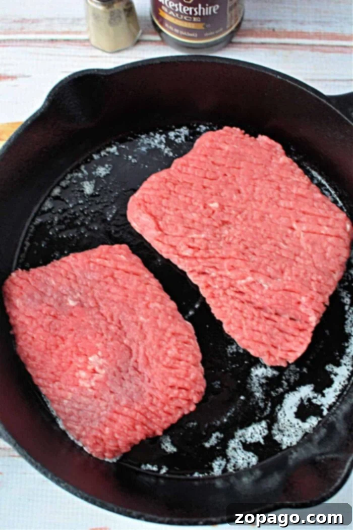 How to Perfectly Pan-Fry Cube Steak 4 Two raw cube steak patties sizzle in a black cast iron skillet, reminiscent of preparing cube steak; timing is key to achieve perfect doneness.