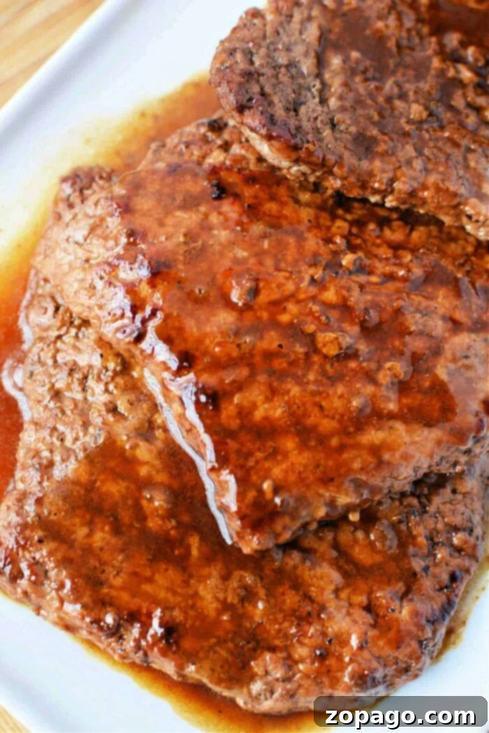 How to Perfectly Pan-Fry Cube Steak 7 Close-up of juicy, cooked cubed steaks in rich brown gravy on a white plate, reminiscent of perfectly timed cube steaks in a frying pan.