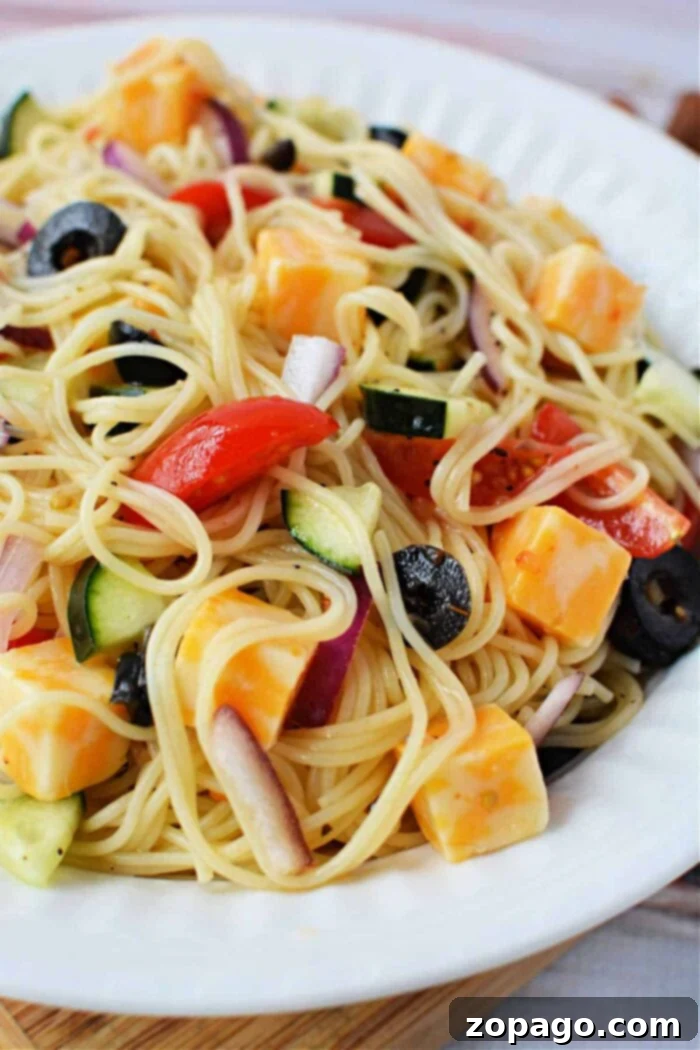 A vibrant plate of 4 Ingredient Pasta Salad featuring angel hair pasta mixed with cherry tomatoes, cucumber, olives, and red onion, tossed in Italian dressing.