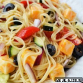 A delightful 4 Ingredient Pasta Salad featuring a plate of spaghetti salad with cheese cubes, sliced olives, tomatoes, red onions, and cucumbers.