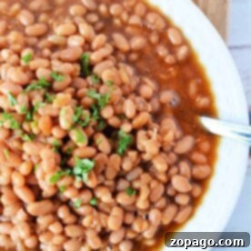 Optimal Bake Time for Baked Beans at 350F 9 A white bowl filled with oven-baked beans, perfectly cooked at 350 degrees, is topped with chopped parsley and placed on a rustic wooden surface.