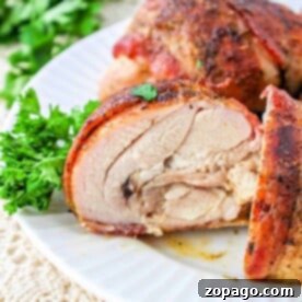 Close-up of seasoned, sliced bacon-wrapped chicken thighs on a white plate, garnished with fresh parsley.