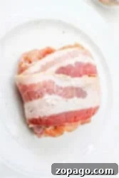 Raw bacon-wrapped chicken thighs rest on a white plate, ready for cooking.
