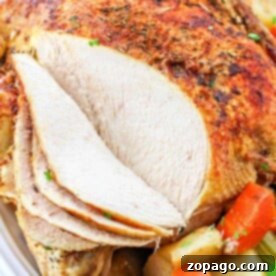 Pot Roast Chicken with a few slices cut, garnished with carrots, potatoes, and herbs on a white plate.