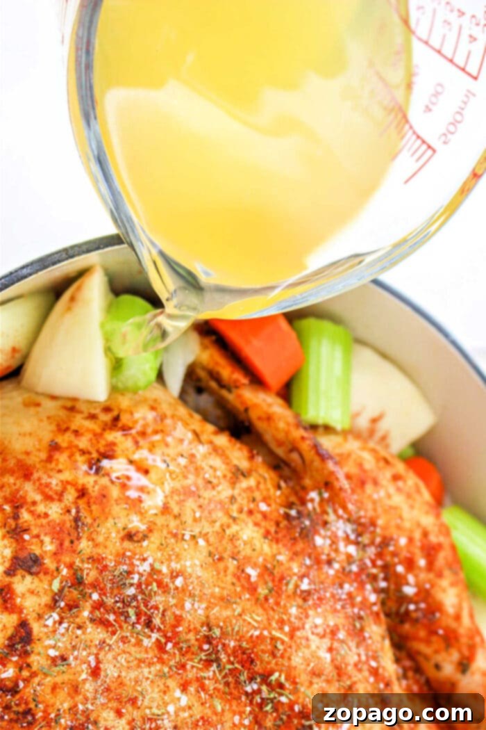 Dutch Oven Roasted Chicken 7 A whole chicken cooked in a pot, ready to be carved and served with its juices and vegetables