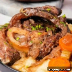 A plate of slow cooker osso buco with tender beef, accompanied by carrots and mashed potatoes, garnished with fragrant herbs.