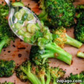 Chinese Broccoli 7 Asian-inspired roasted broccoli on a tray with a spoonful of savory dressing being drizzled over it.