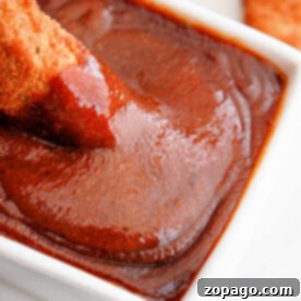chicken being dipped into rich, popeyes barbecue sauce in a white bowl
