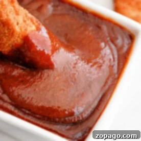 Chicken being dipped into rich, homemade Popeyes barbecue sauce in a white bowl