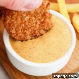 A hand dips a chicken nugget into creamy dipping sauce, reminiscent of those signature flavors you'd find when learning how to make Burger King sauces, with crispy fries in the background on a wooden board.