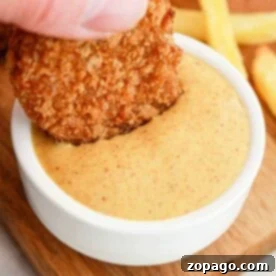 A hand dips a chicken nugget into creamy dipping sauce, reminiscent of those signature flavors youd find when learning how to make Burger King sauces, with crispy fries in the background on a wooden board.