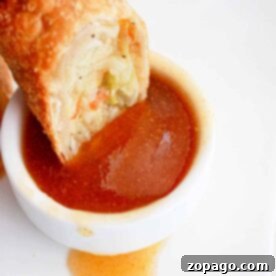 An egg roll gracefully meets its match as its dipped into a small white bowl brimming with rich egg roll sauce, all set on a pristine white plate.