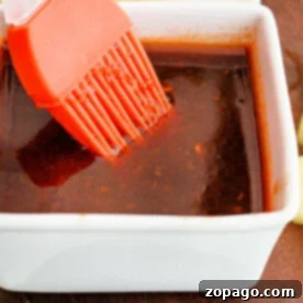 Perfect Huli Huli Sauce at Home 7 A square white dish holding Huli Huli Sauce, complemented by an orange basting brush resting inside.